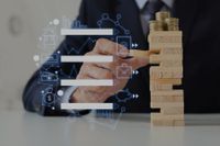 Hombre de traje juega a Jenga con monedas encima de la torre Hombre de traje juega a Jenga con monedas encima de la torre